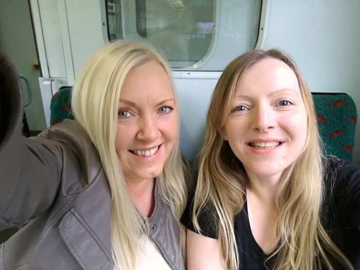 Two girls smiling, with fair hair, taking a selfie on the train
