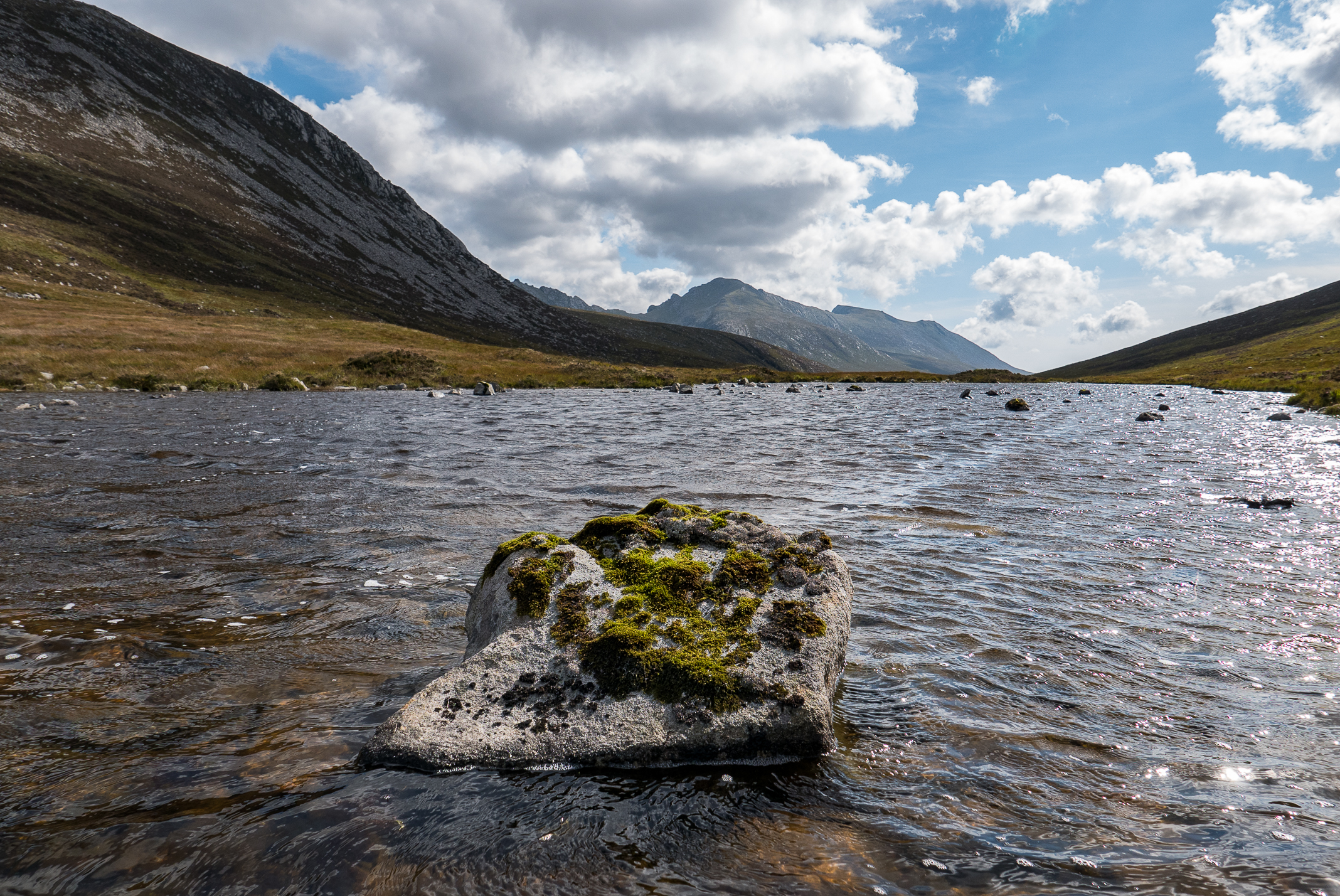 Moss covered rock sitting in Loch na Davie with mountain views