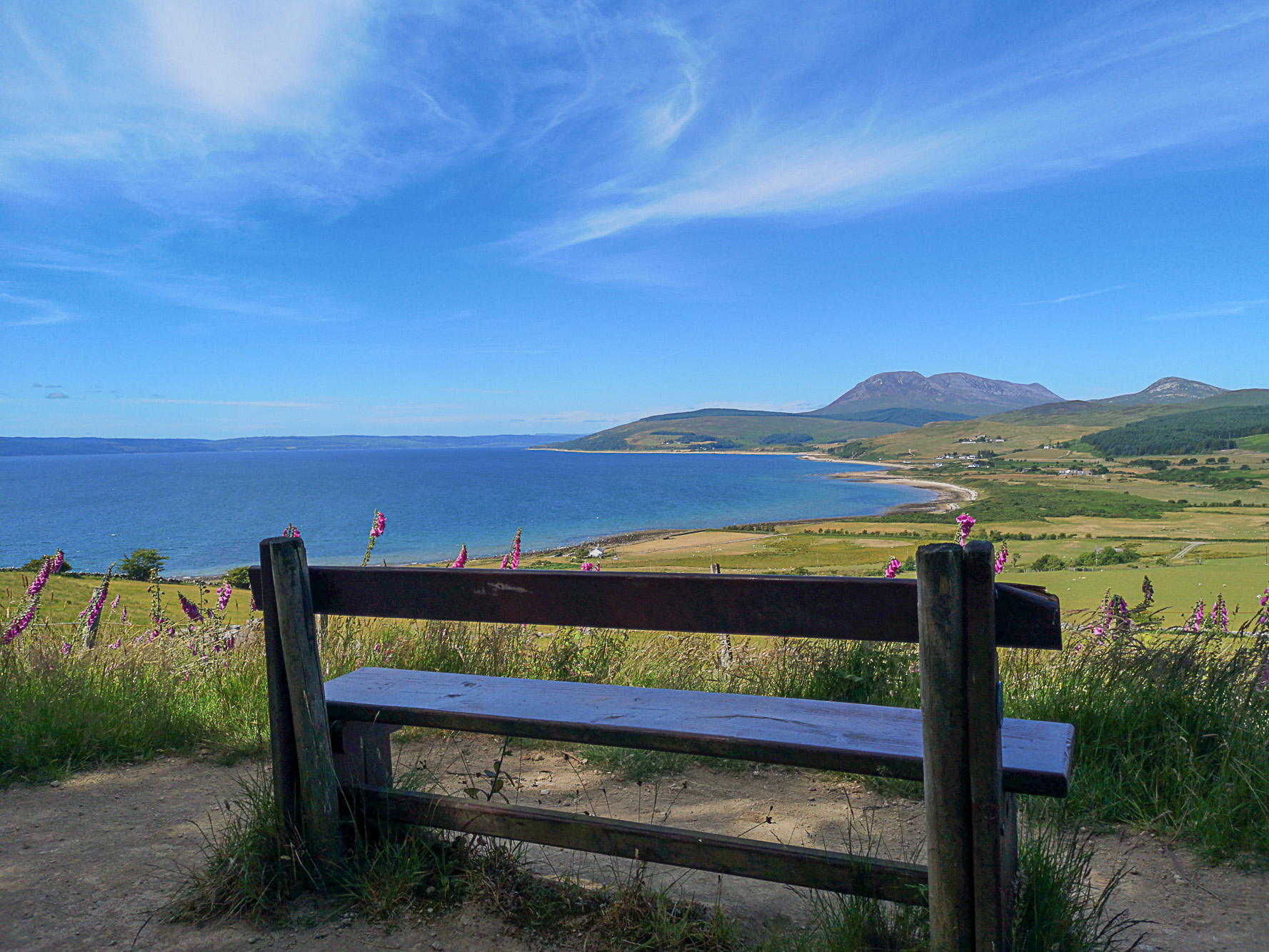 Bench with a view across the lush green landscape, blue ocean and hills in the distance