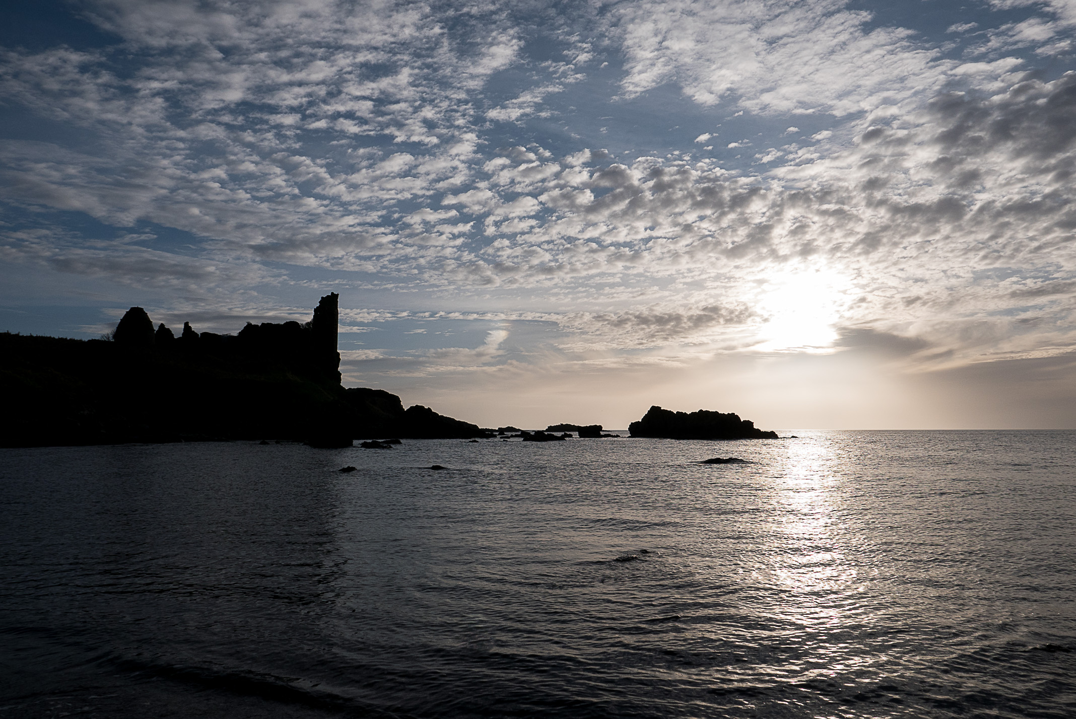 Calm ocean lit up by the sun setting, black sillouette of Dunure Castle and rocks